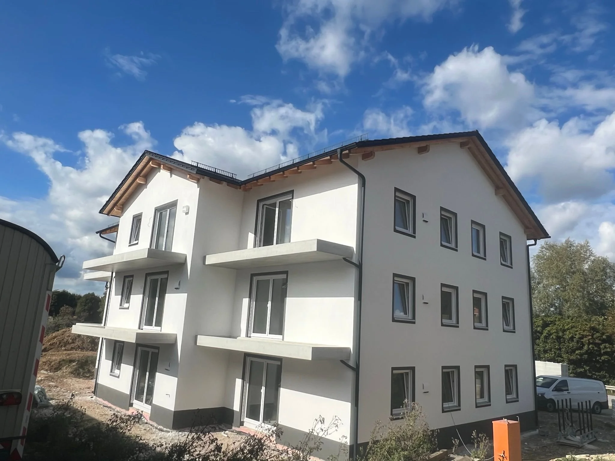 Neues weißes Mehrfamilienhaus mit Balkonen, vier Stockwerke, unter construction, blauer Himmel mit Wolken