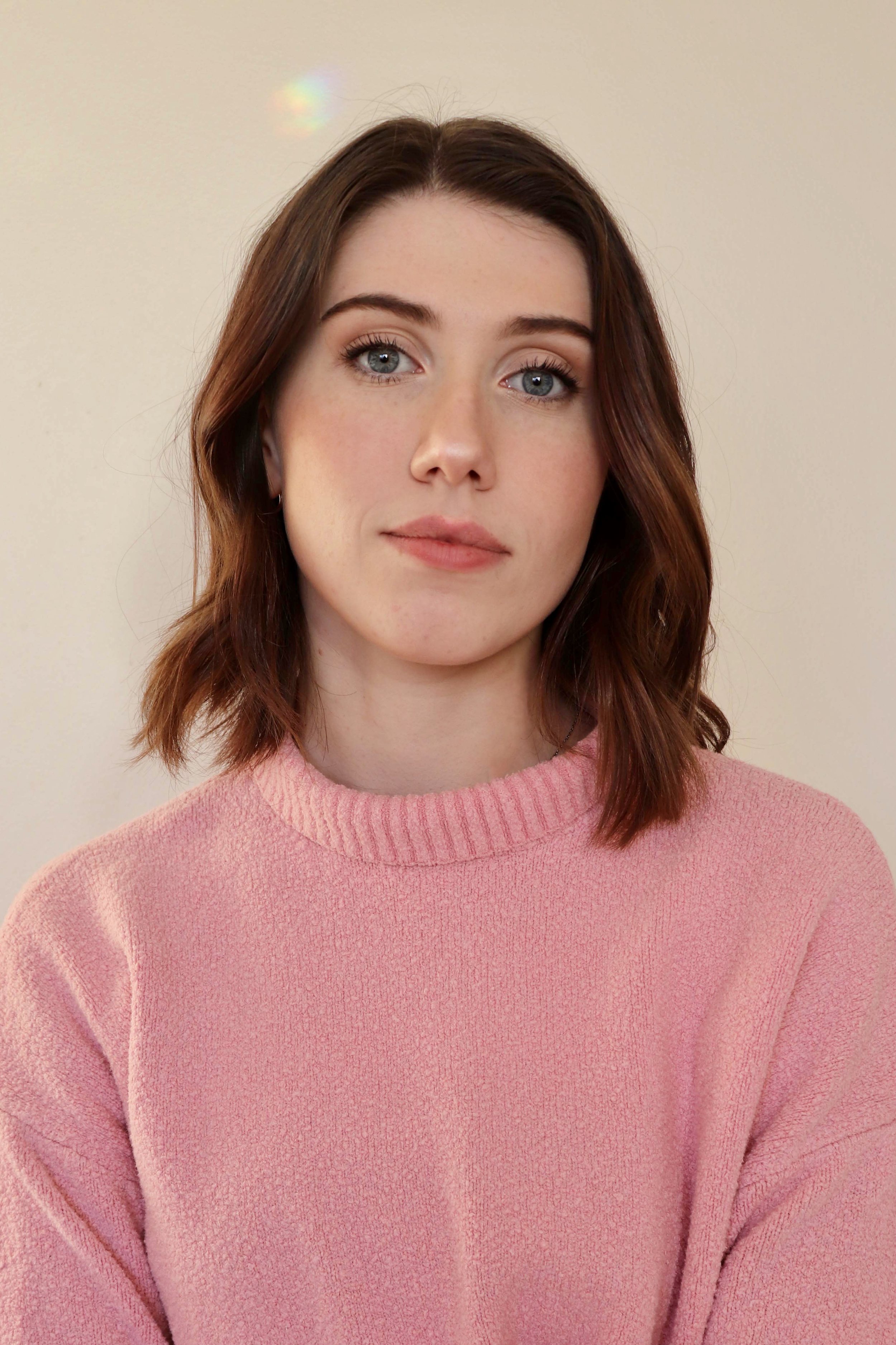 Person with brown hair wearing a pink sweater against a plain background.
