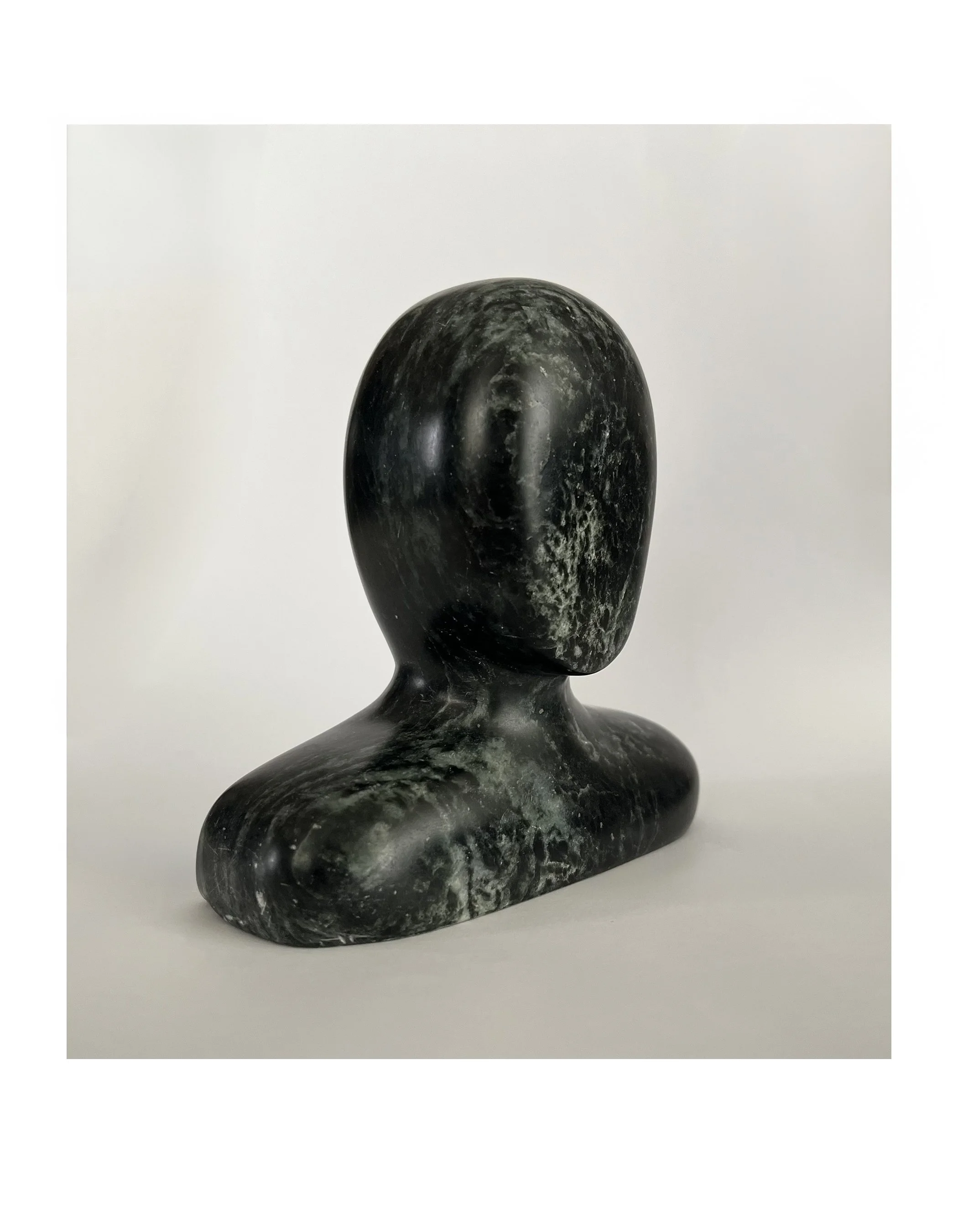Abstract marble sculpture of a human bust with smooth, featureless surface and dark green coloration.