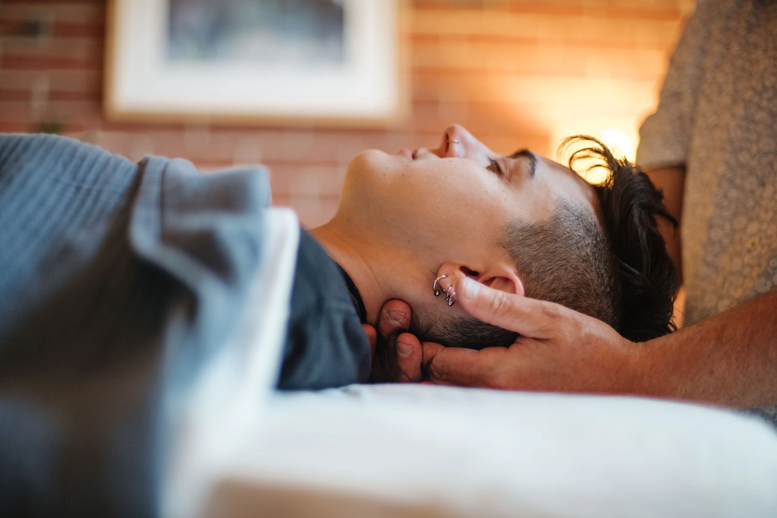 Person receiving a neck and head massage on a couch in a cozy room with a brick wall and framed picture in the background.
