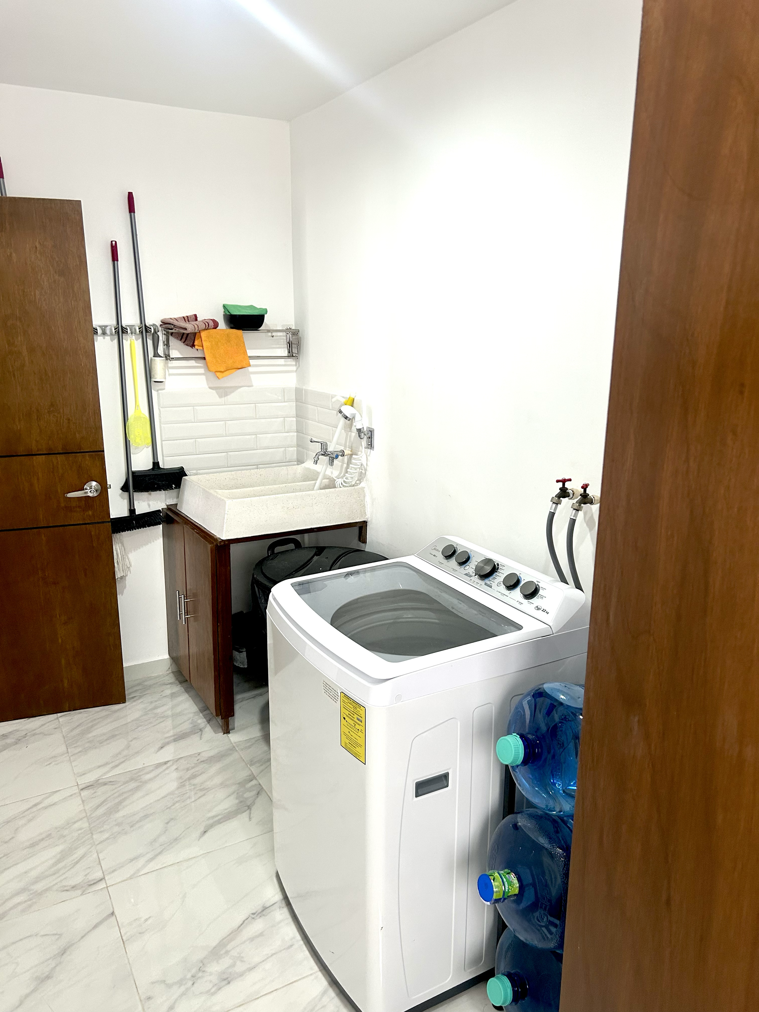 Laundry room with washing machine, water bottles, sink, cleaning supplies, and storage cabinet.