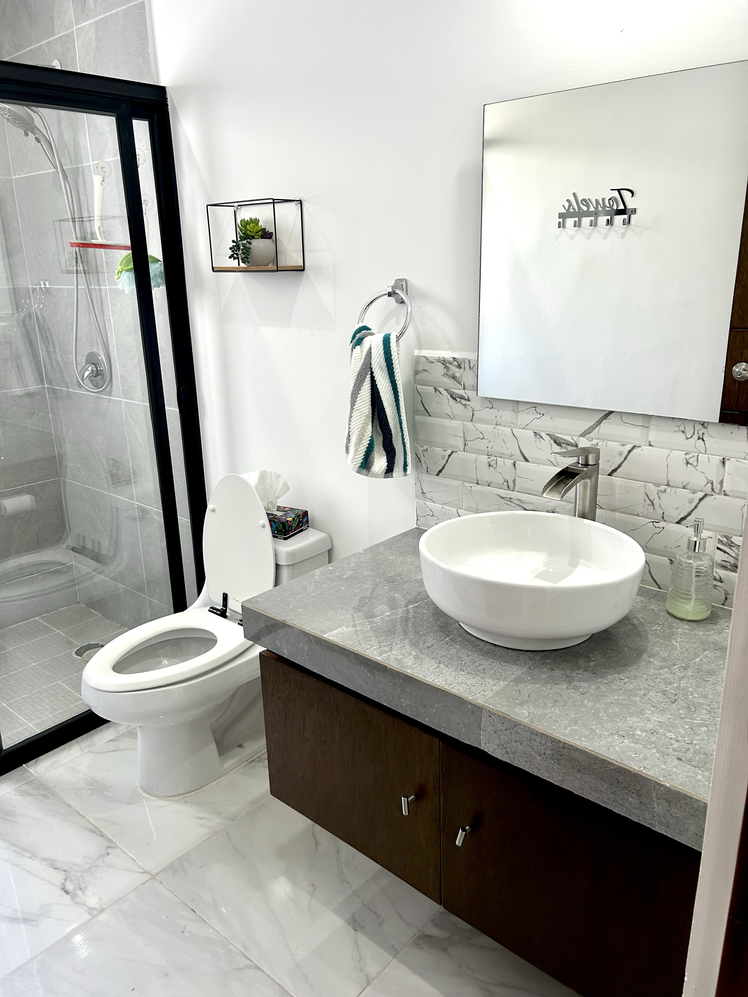 Modern bathroom with a shower, toilet, and a vanity with a round vessel sink and marble backsplash.