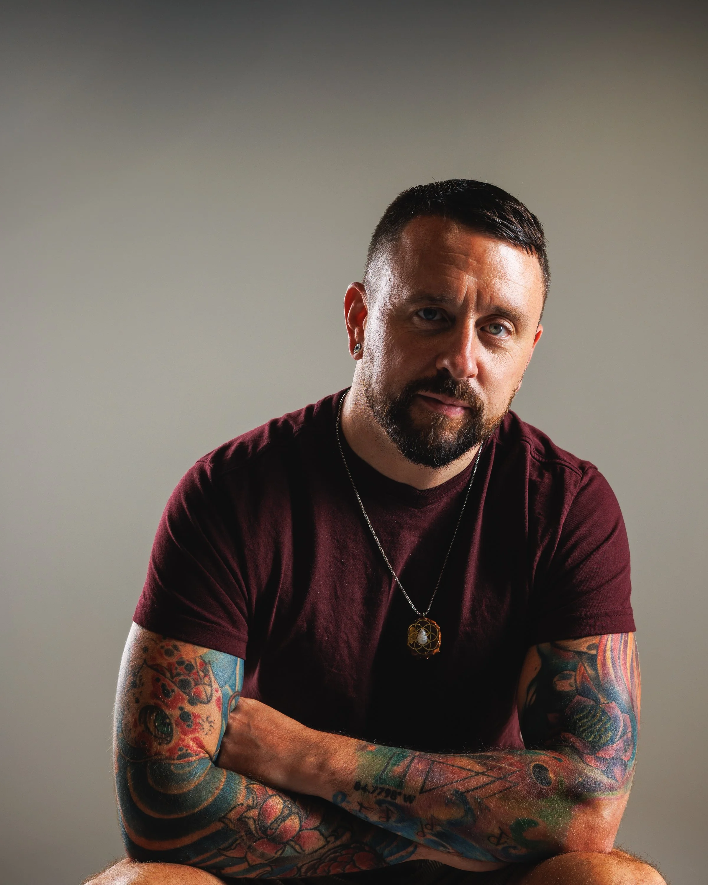 Denver personal branding portrait with clean directional lighting, relaxed expression, tattoos, neutral studio tones, and professional imagery for websites, profiles, and marketing.