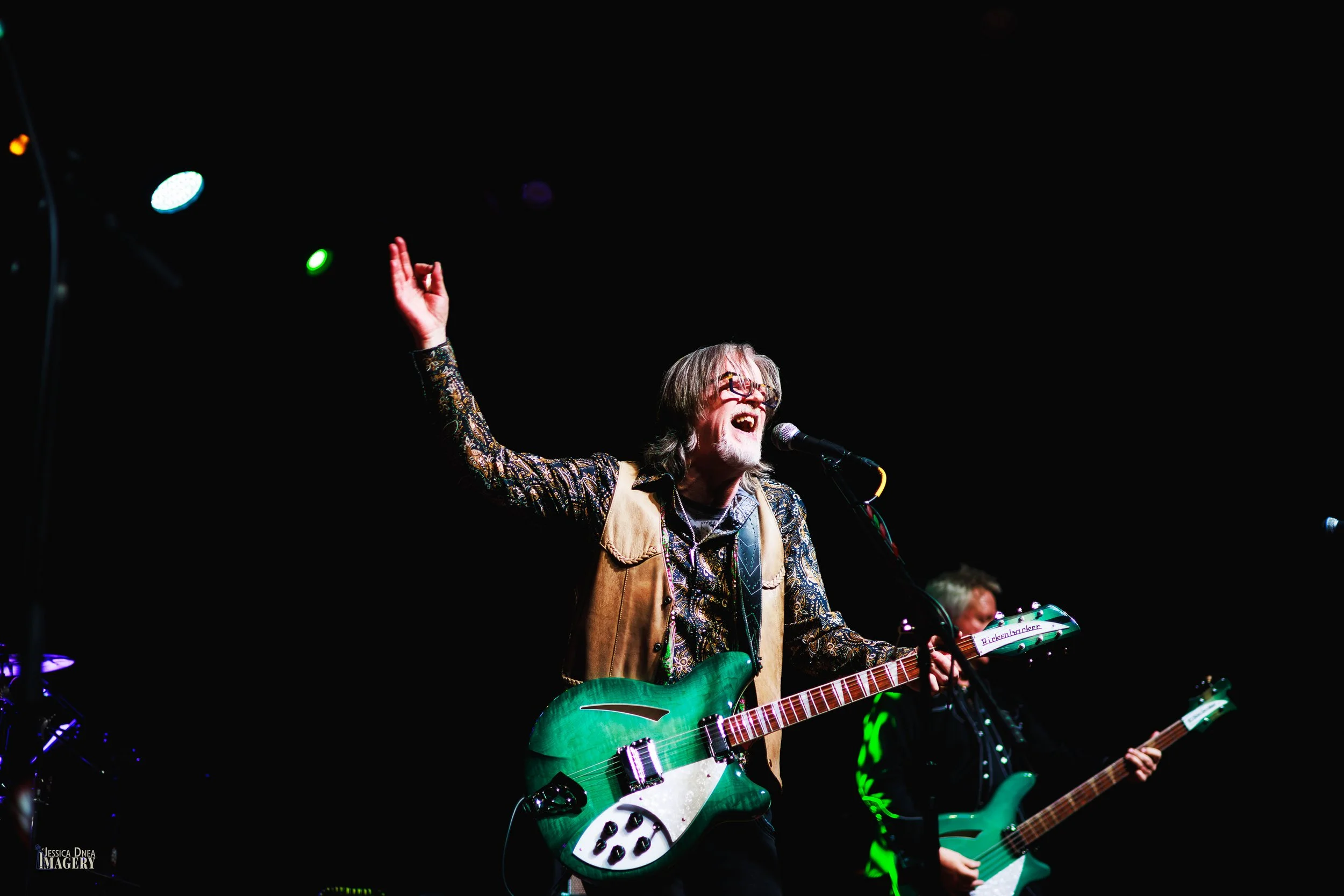 Patrick Dune’s singer raises one hand while performing with a green guitar beneath colorful lights during a 2026 Denver concert.