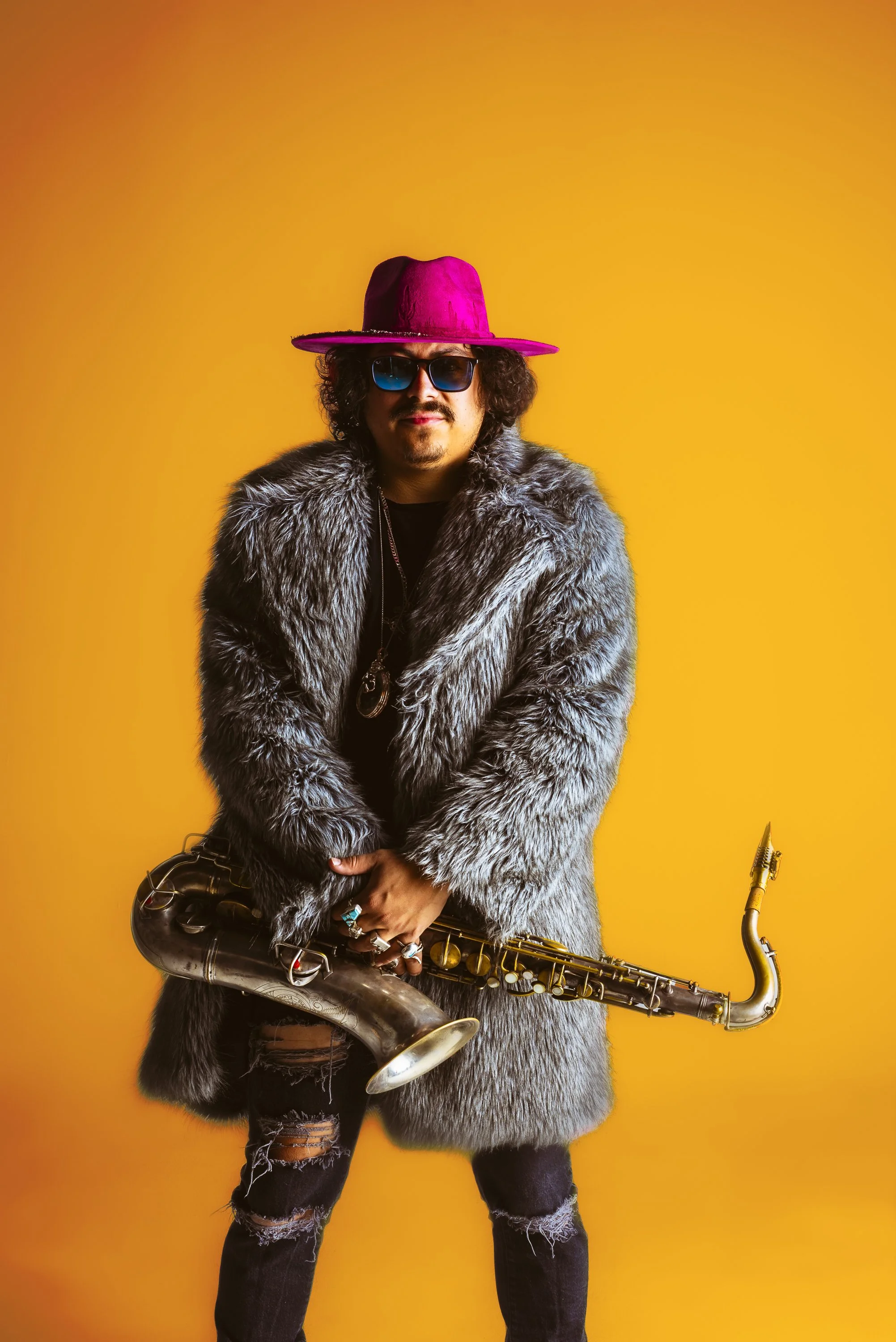 Musician press portrait with a saxophone, faux-fur coat and bold orange background created from a white cyc studio image.