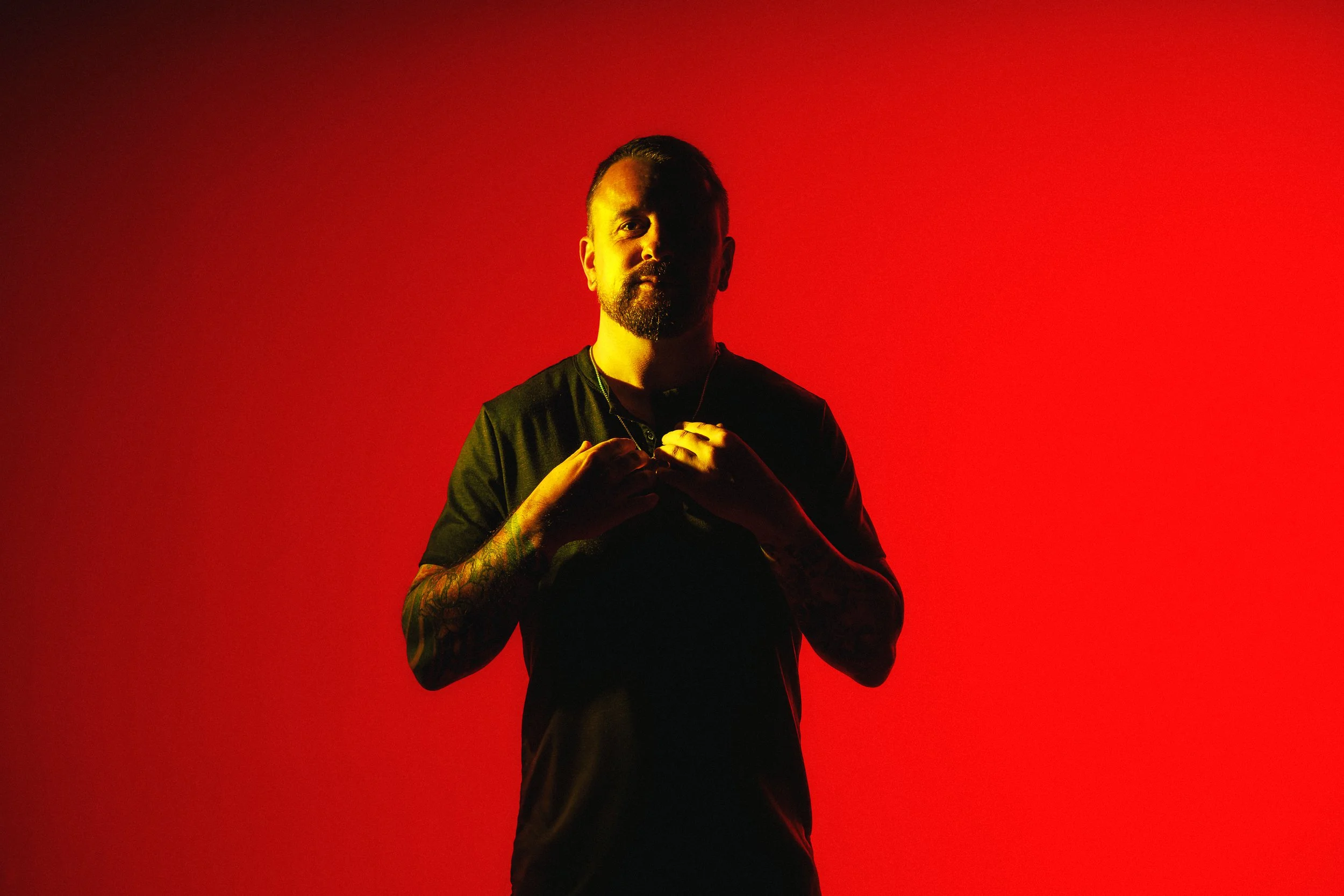 Dramatic musician promo portrait with red background lighting and warm highlights for EPK and release promotion.