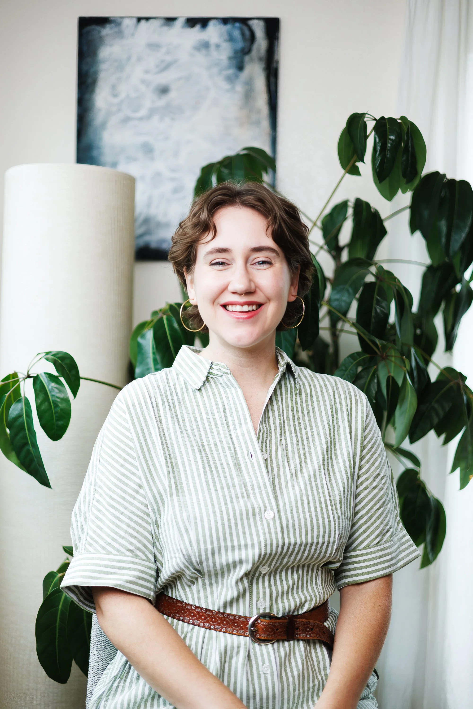 Smiling professional in a green striped outfit seated beside plants during a clean lifestyle branding portrait session by Jessica Dnea Imagery.