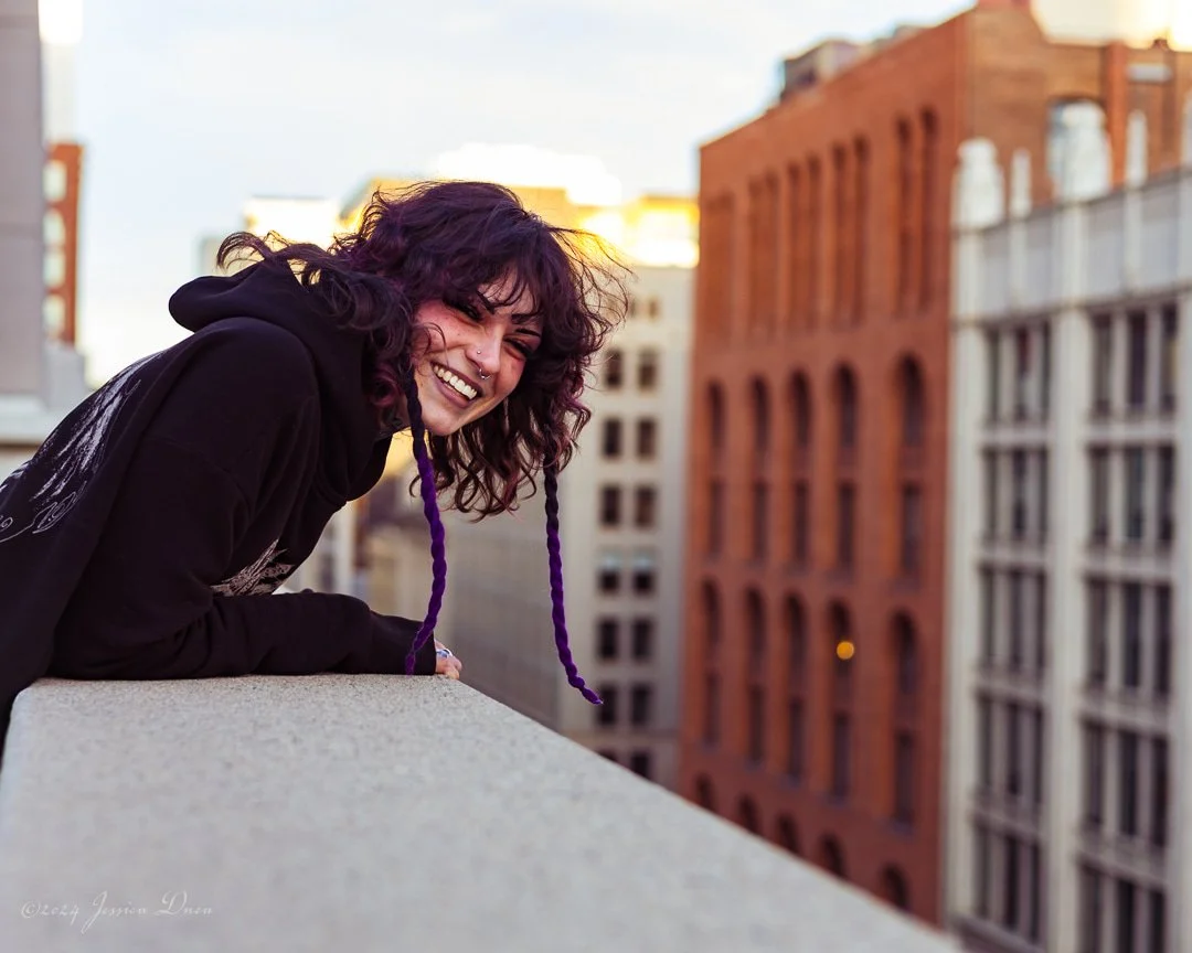 Creative professional with purple hair laughing on a downtown rooftop during an expressive Denver branding photography session by Jessica Dnea Imagery.