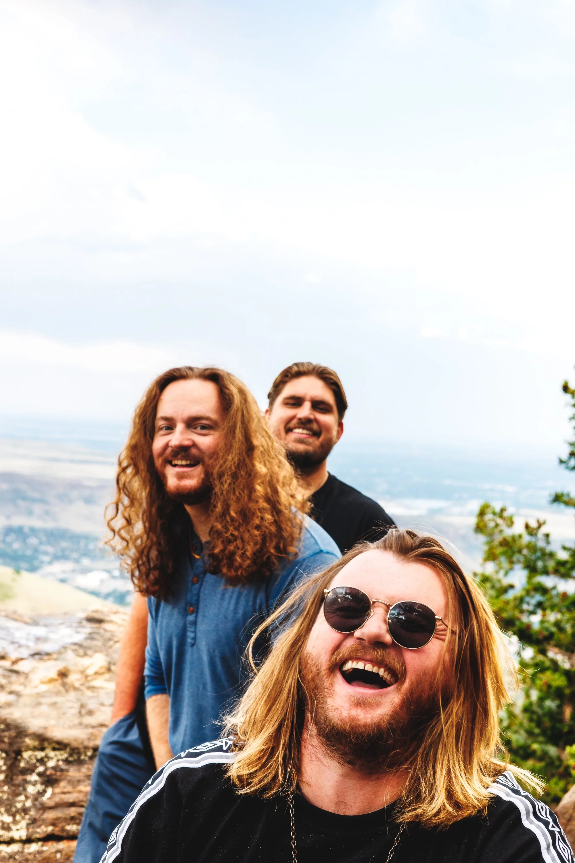 Candid on-location press photo of three RADO band members laughing at a Colorado mountain overlook.