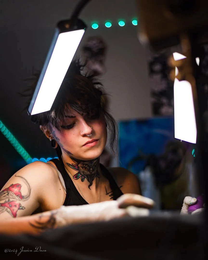 Tattoo artist concentrating beneath studio task lights during a process-focused personal branding session by Denver photographer Jessica Dnea Imagery.