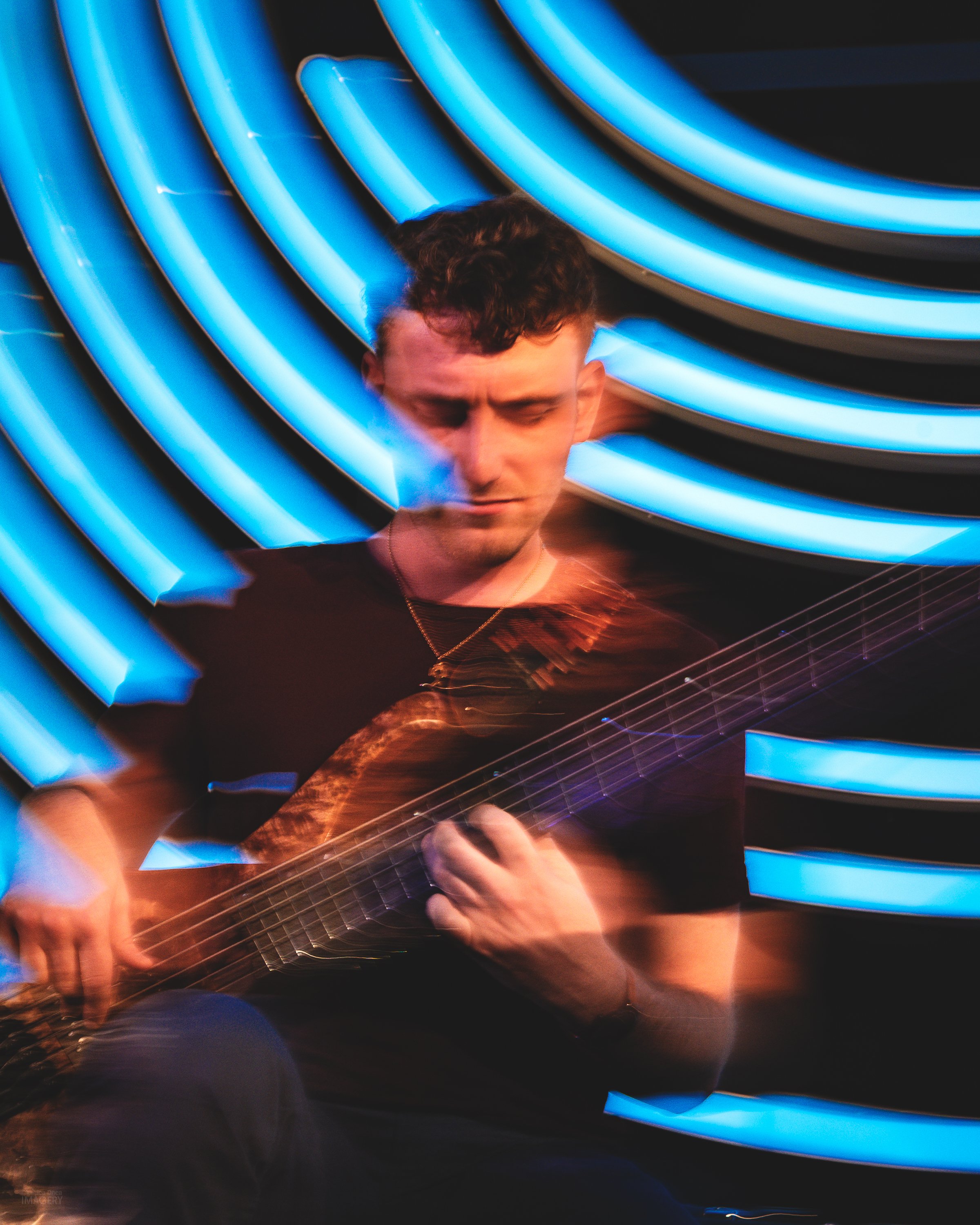 Creative motion blur surrounds a Chick Magnet bassist performing against illuminated blue circles at Dazzle Denver.