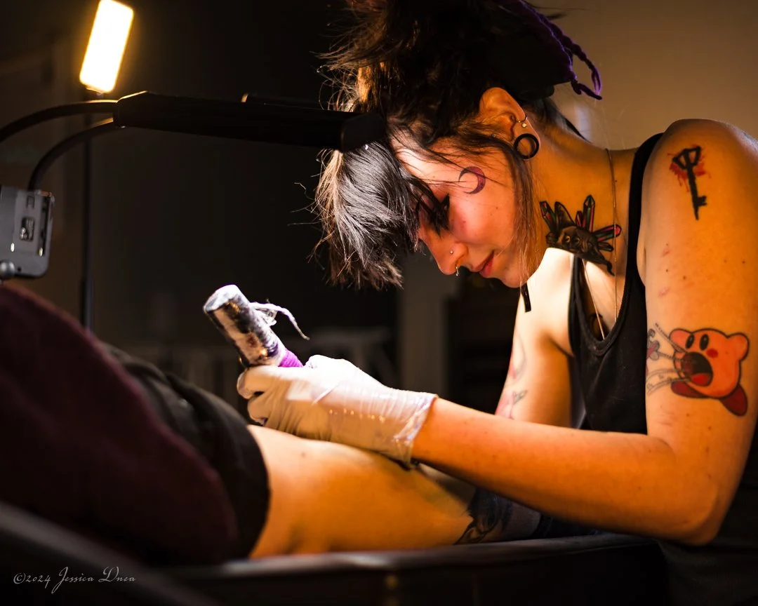 Side-view process photograph of a tattoo artist concentrating while working with a client in her professional studio environment.