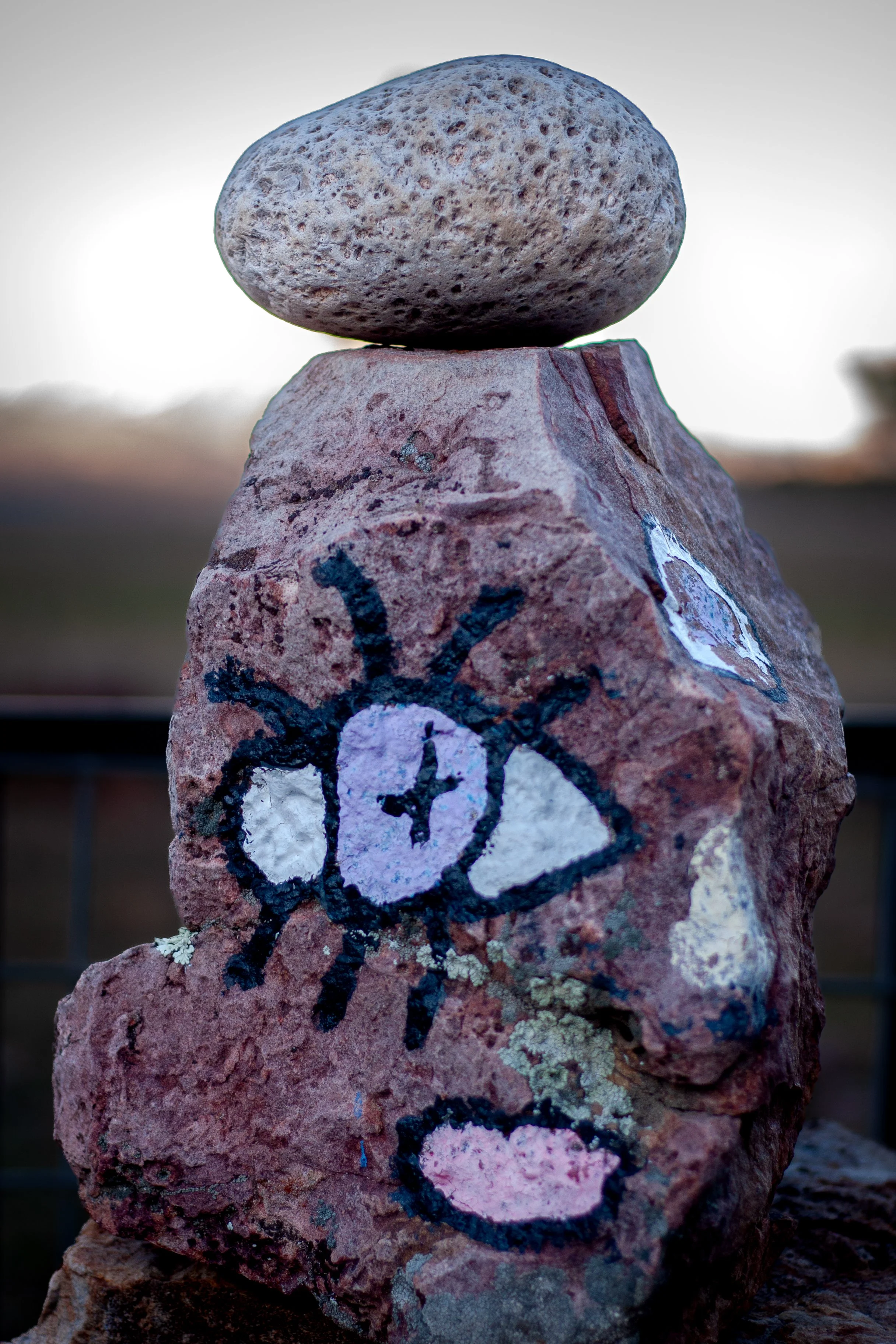 A stack of rocks with a small painted illustration of a unicorn with a purple horn and pink heart on the side of the larger stone.