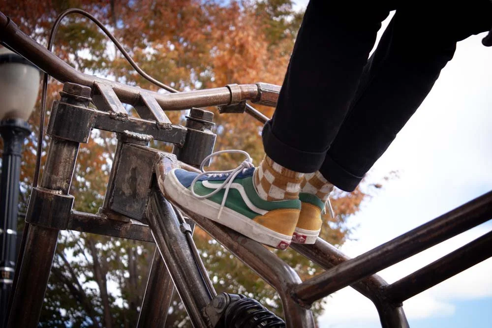 Person wearing colorful sneakers and checkered socks sitting on a metal structure with autumn leaves in the background.