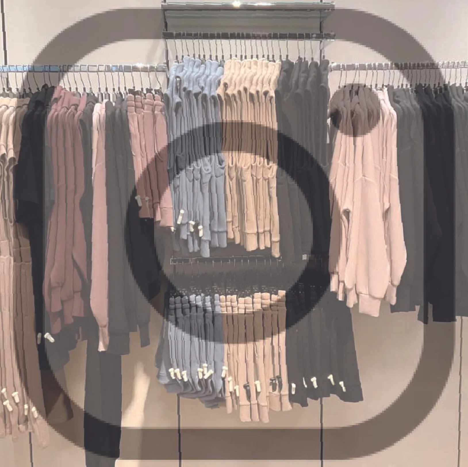 Clothing rack with folded and hanging sweaters and hoodies in beige, gray, pink, black, and beige colors in a retail store.