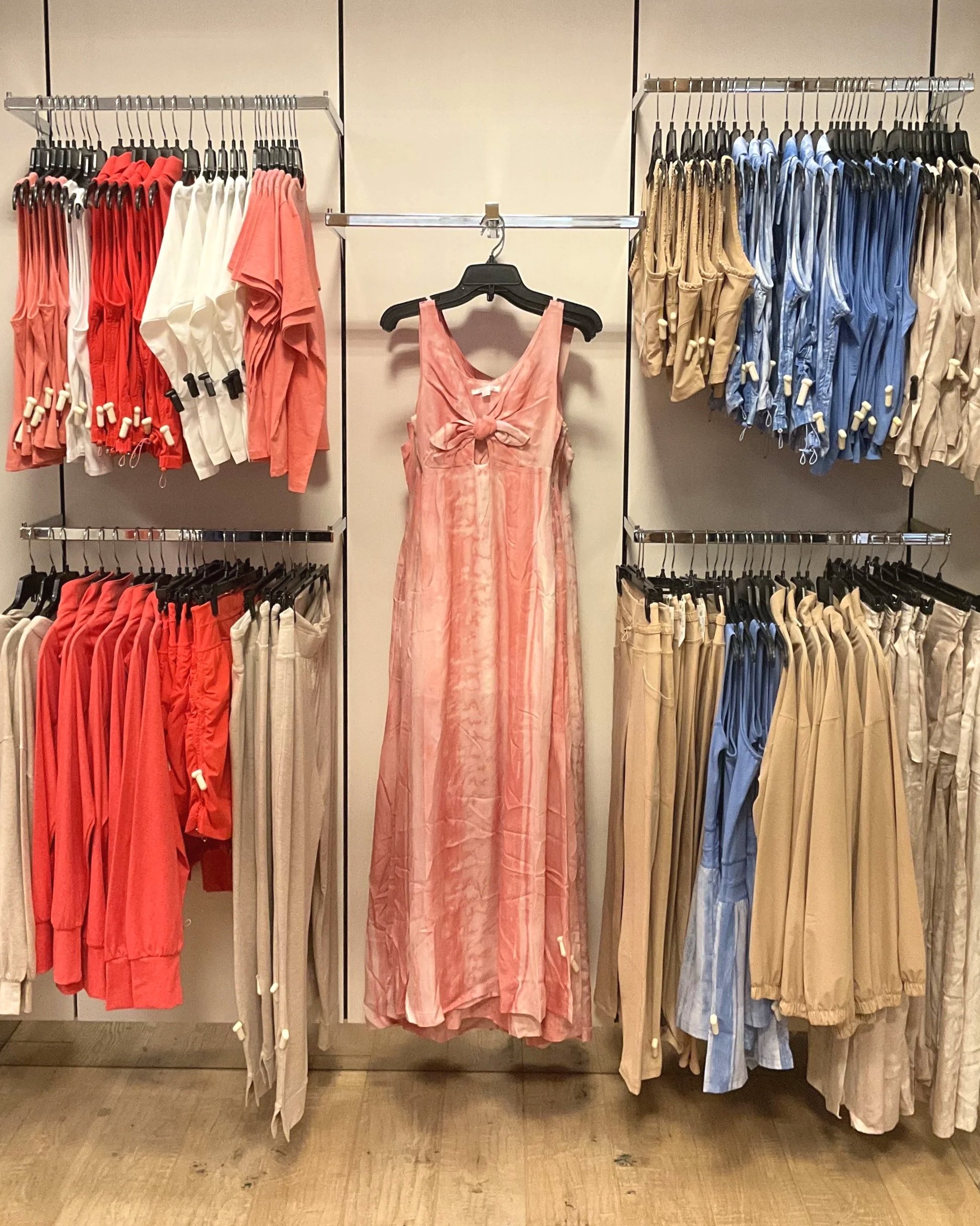 Pink dress hanging in the center of a retail display, surrounded by racks of clothing in various colors including red, beige, blue, and white.