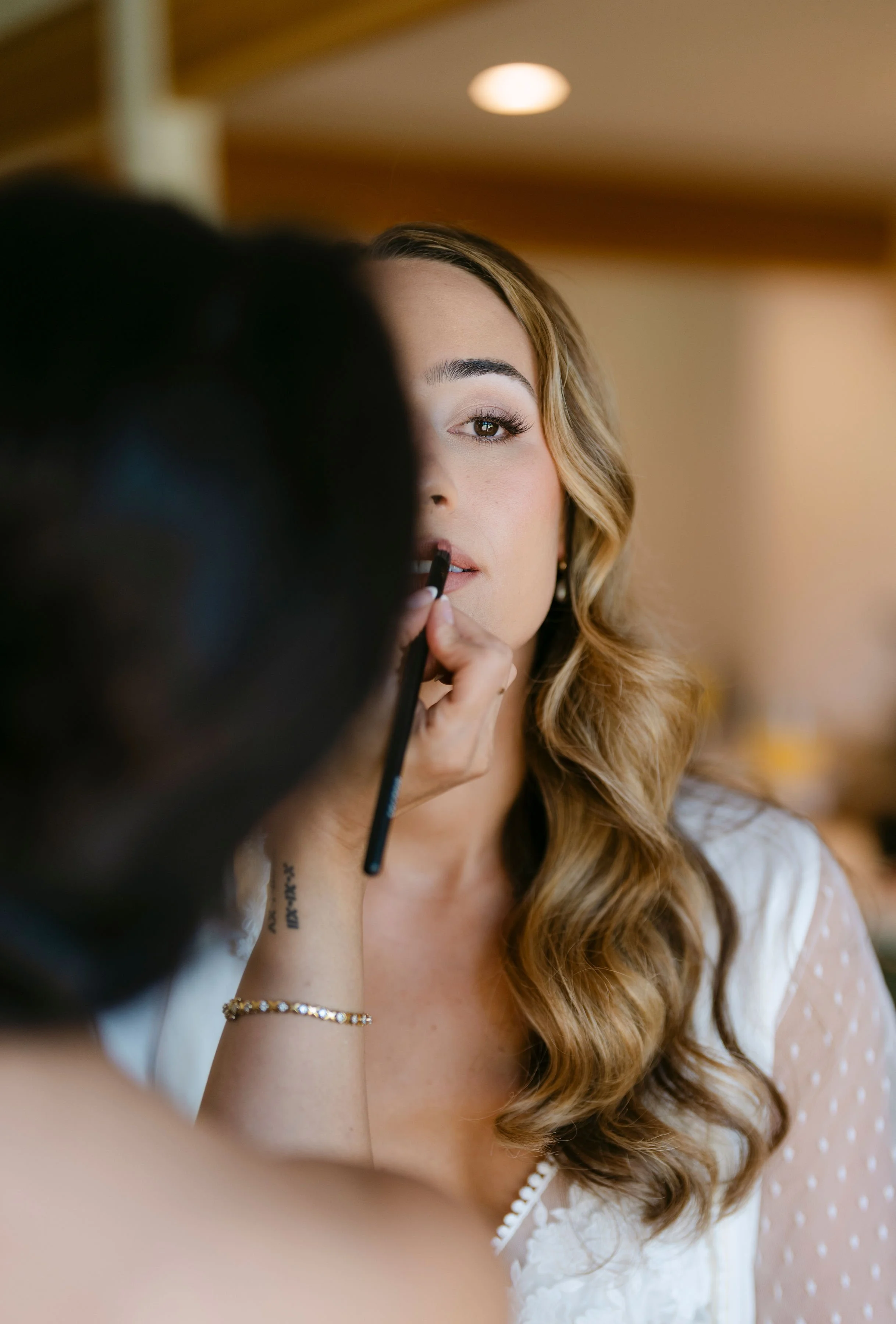 A woman with long wavy hair getting her makeup done by a makeup artist.