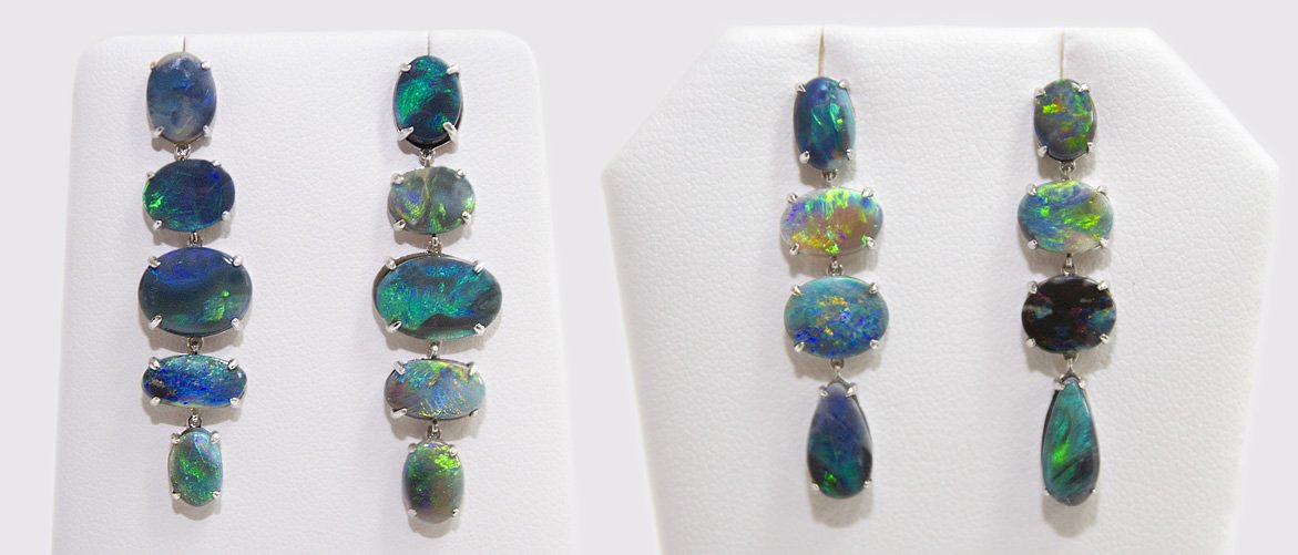 Two pairs of earrings with black opal gemstones displayed on white jewelry stands.