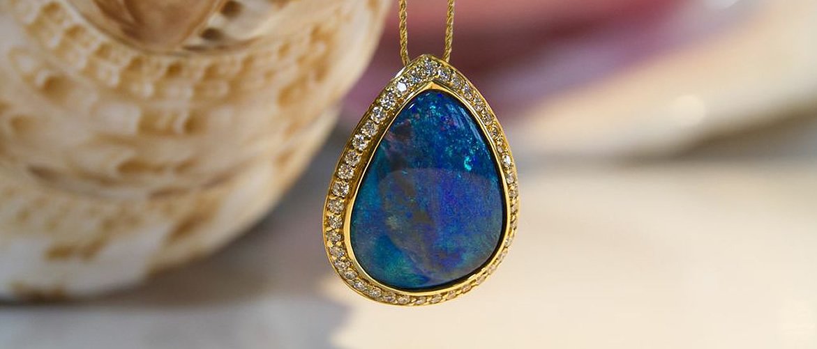 A teardrop-shaped pendant with an opal stone surrounded by small diamonds, hanging from a gold chain.