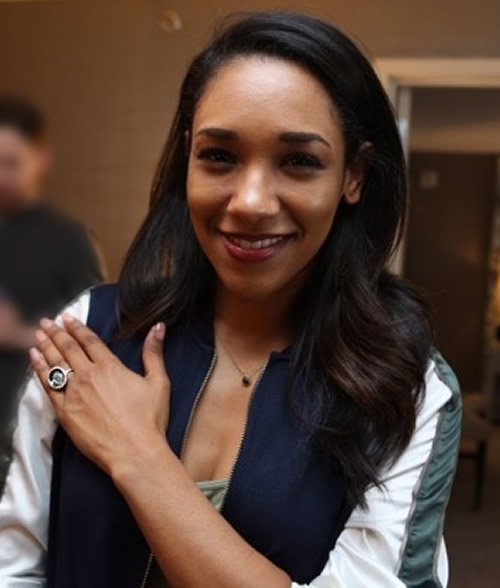 Smiling woman with dark hair, wearing a navy and white jacket, standing indoors.
