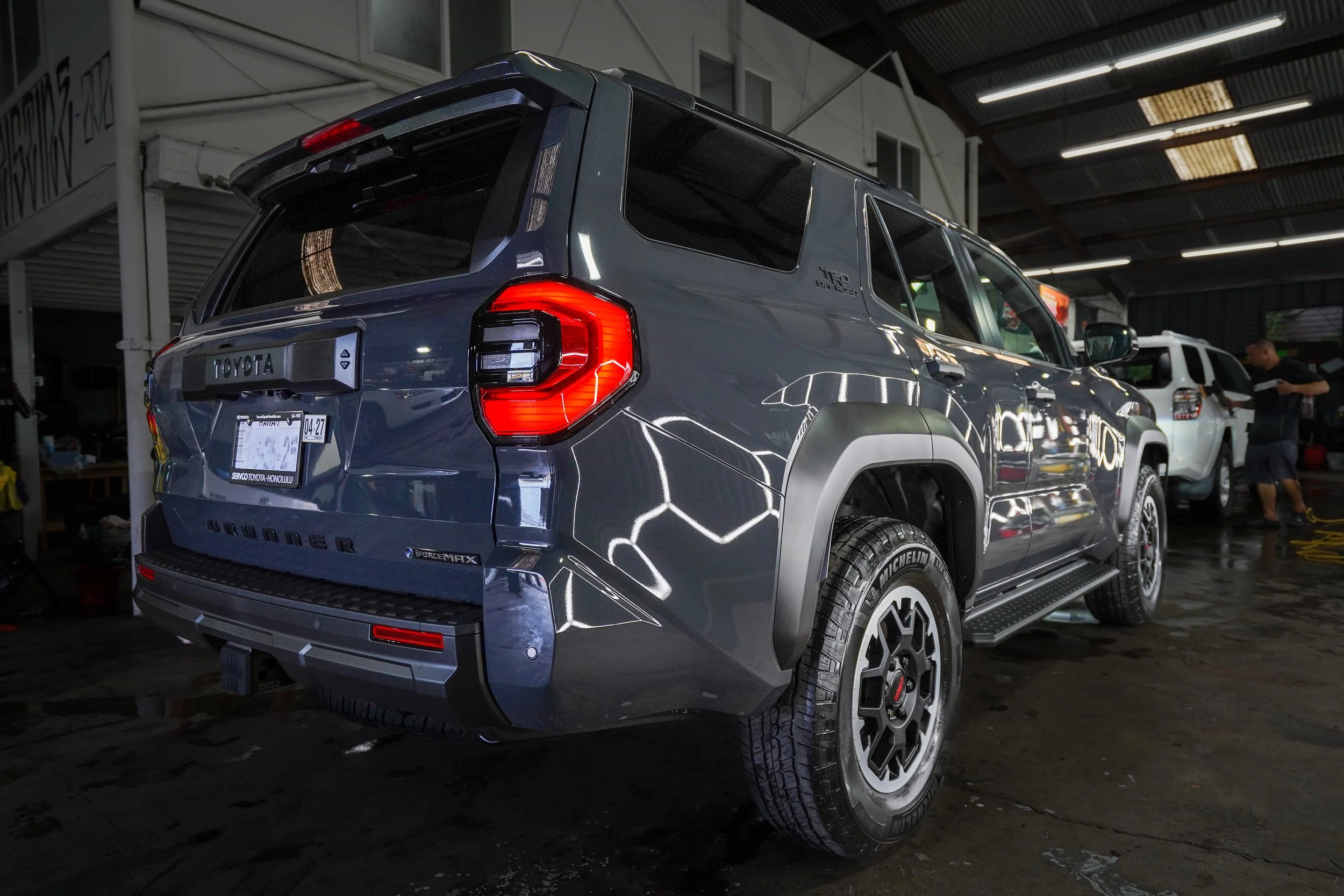 A dark gray Toyota SUV inside a garage, with reflected lighting on its surface, and another white SUV in the background.