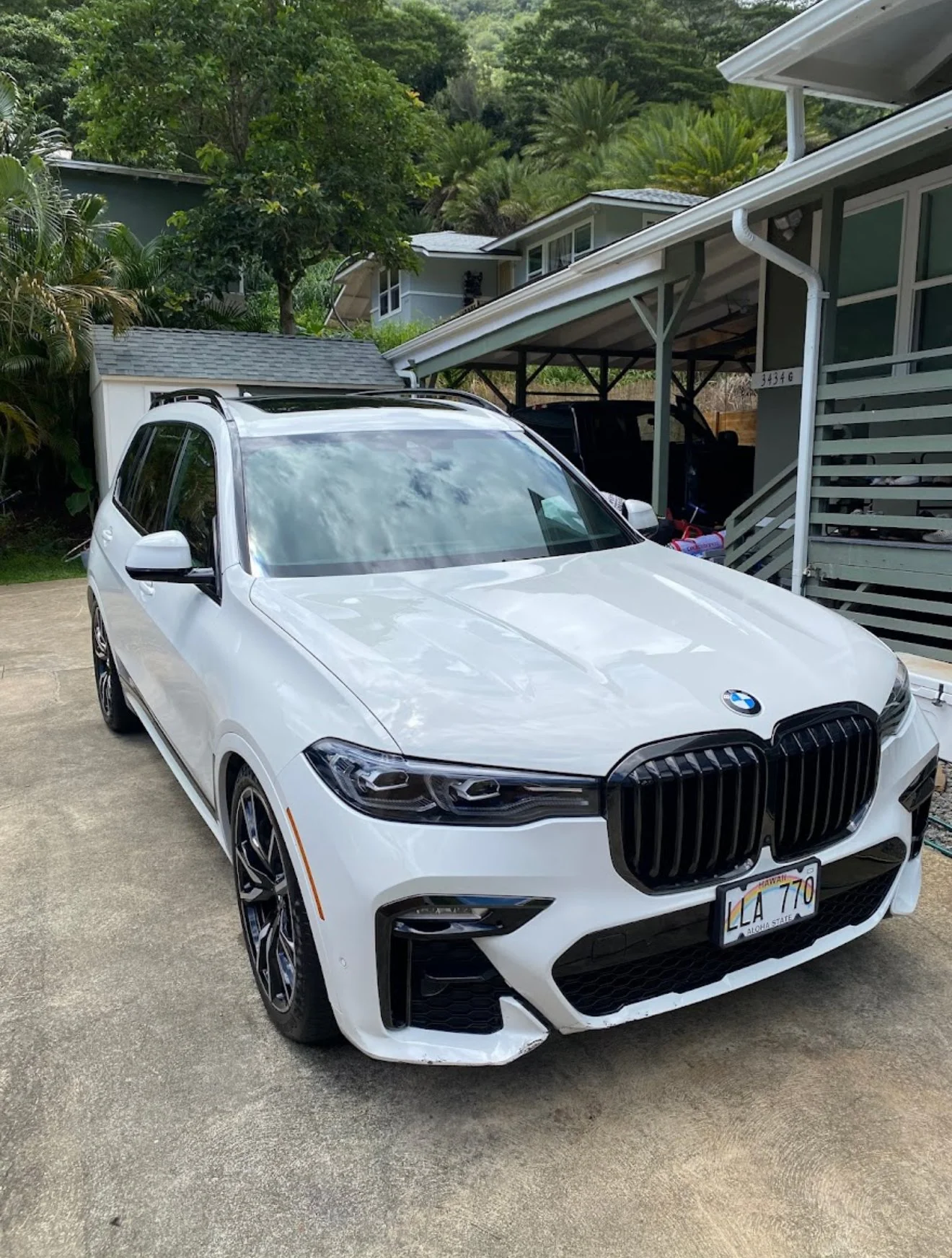 White BMW SUV parked in driveway with damage on the front bumper's right side.