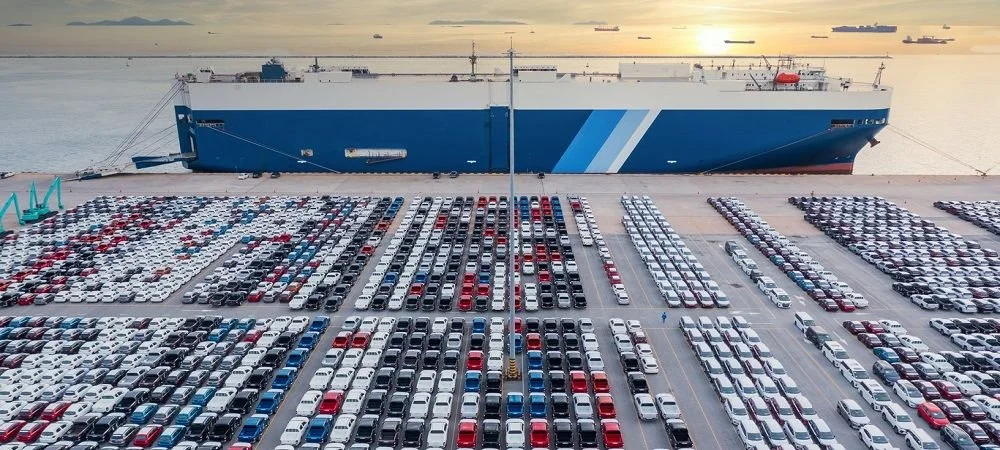 Large shipping vessel docked near a parking lot filled with rows of parked cars