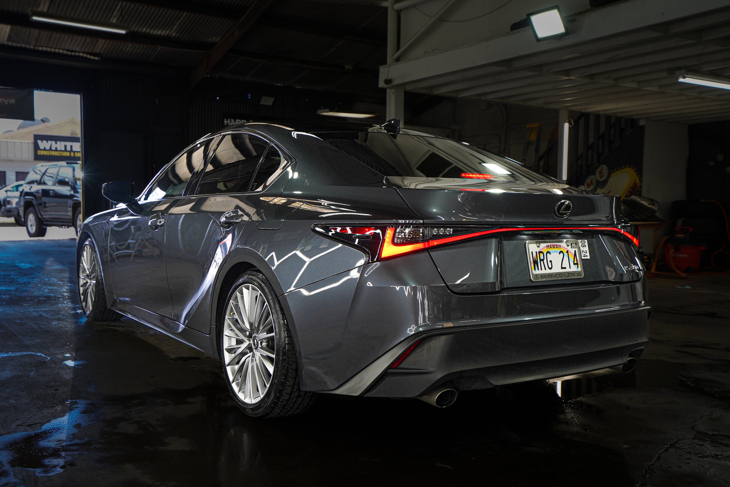 Dark gray Lexus sedan inside a garage with a Hawaii license plate and reflections on its surface.
