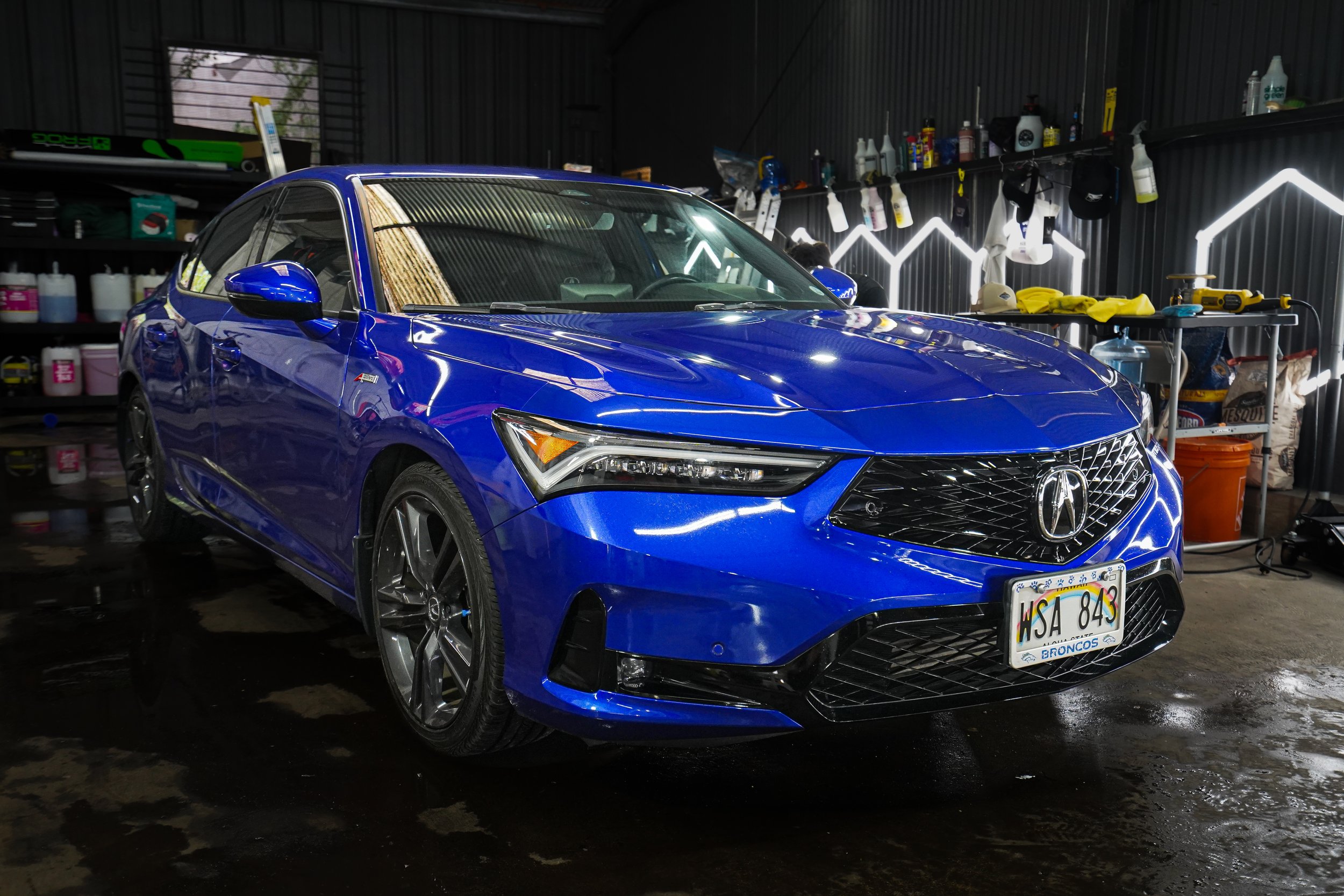 Blue Acura sedan parked inside a garage with cleaning supplies and tools in the background.
