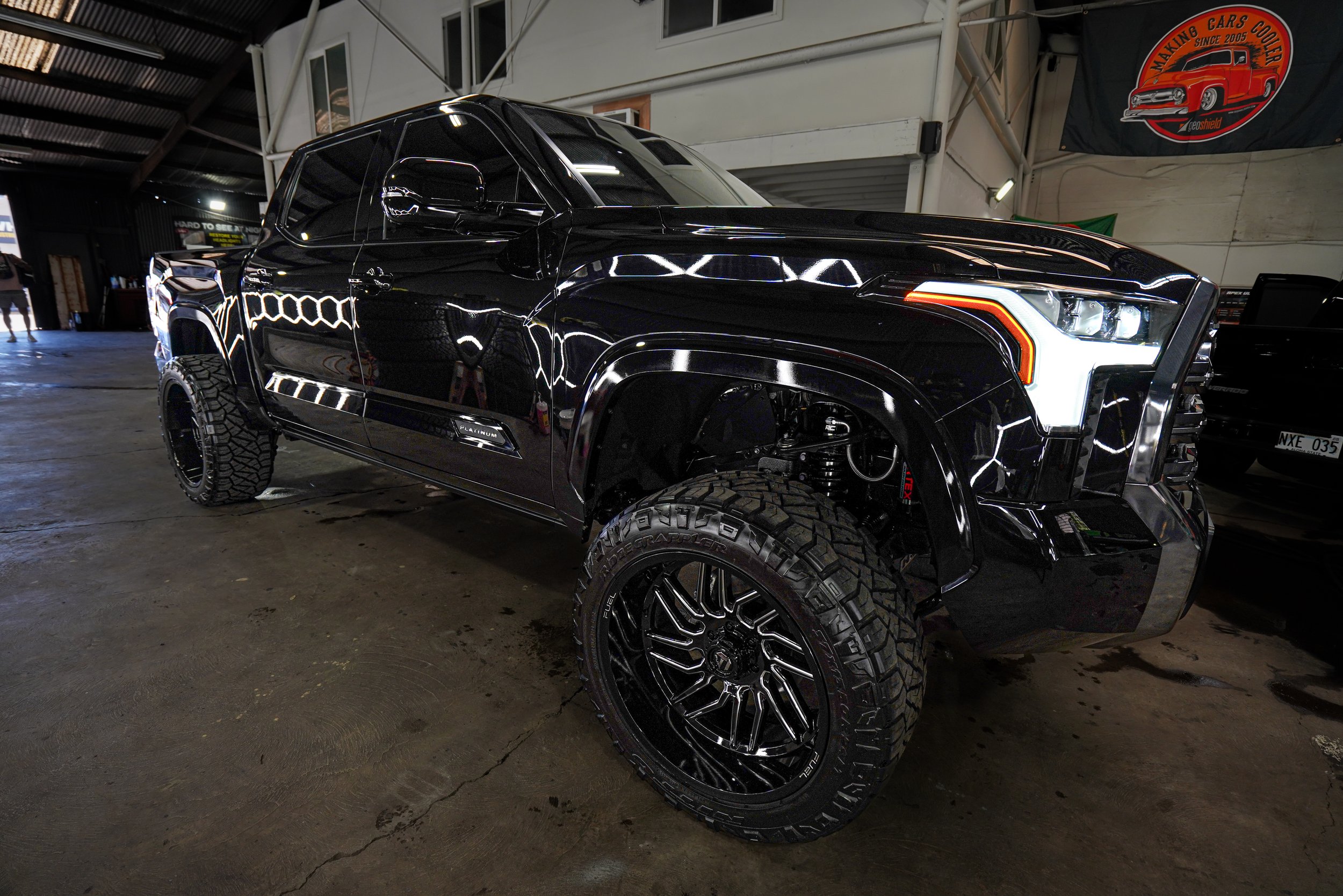 A black pickup truck with large off-road tires and tinted windows parked inside a garage or warehouse.