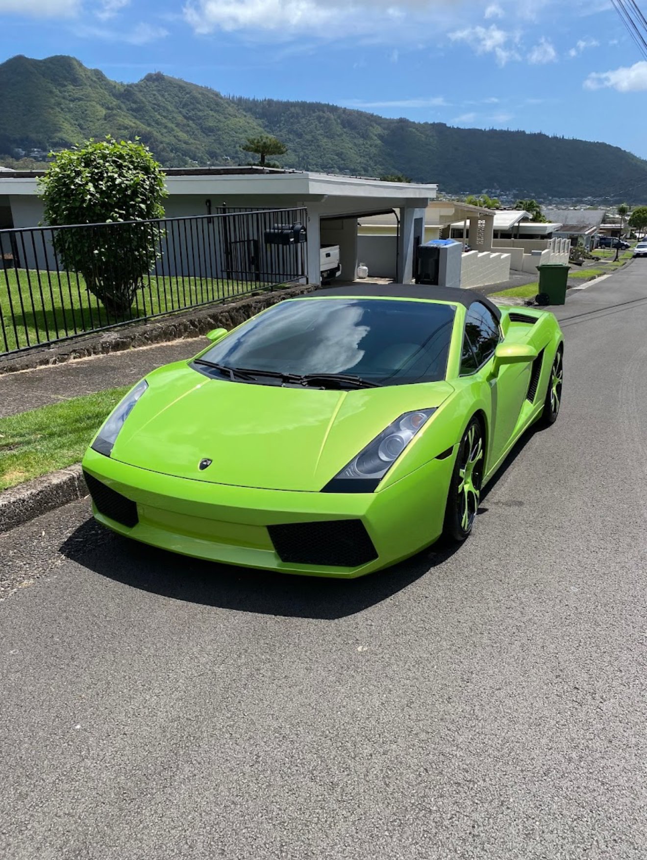 Bright green Lamborghini Gallardo parked on a residential street with mountains in the background.