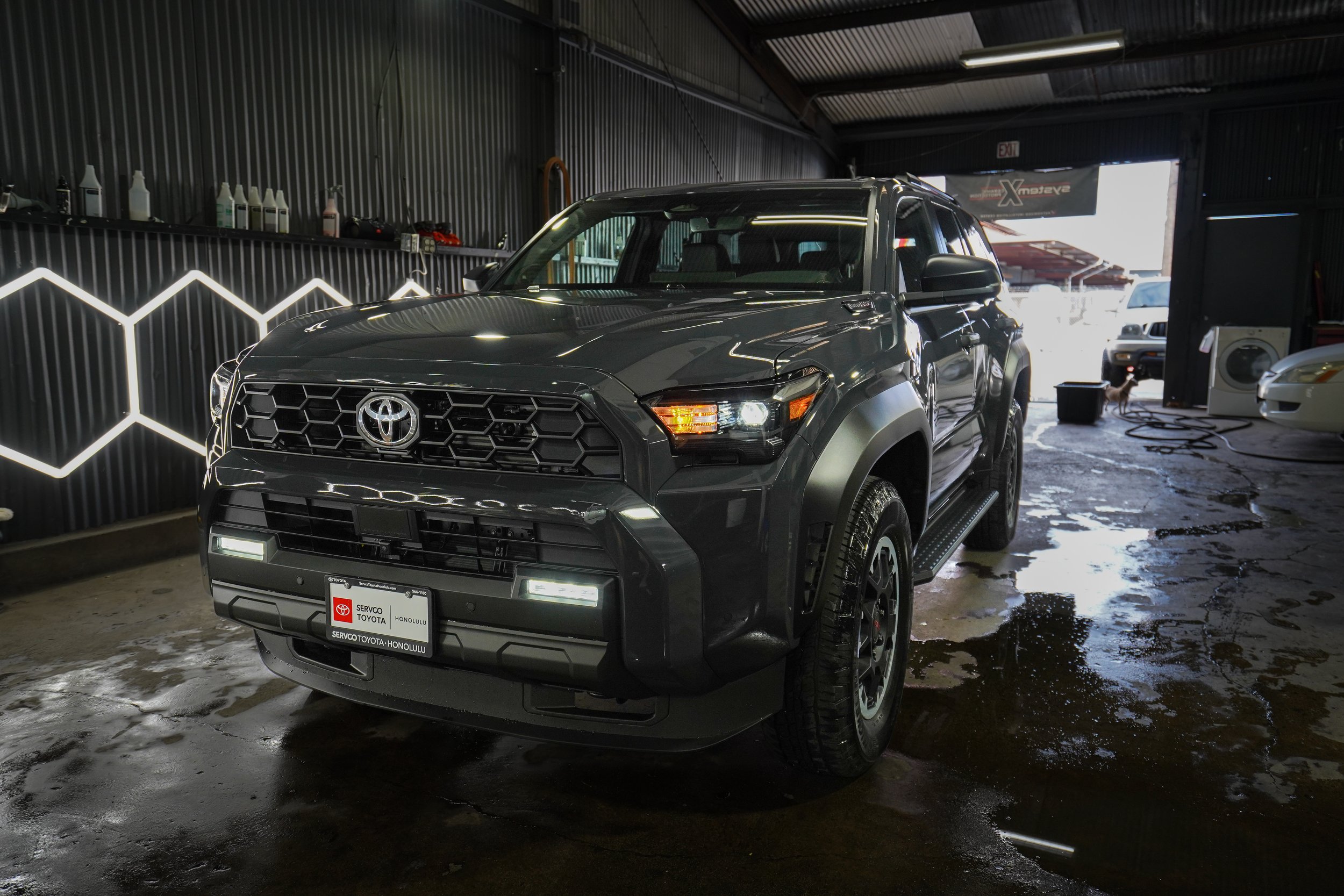 Gray Toyota SUV parked inside a car wash with wet floor and washing supplies on shelves