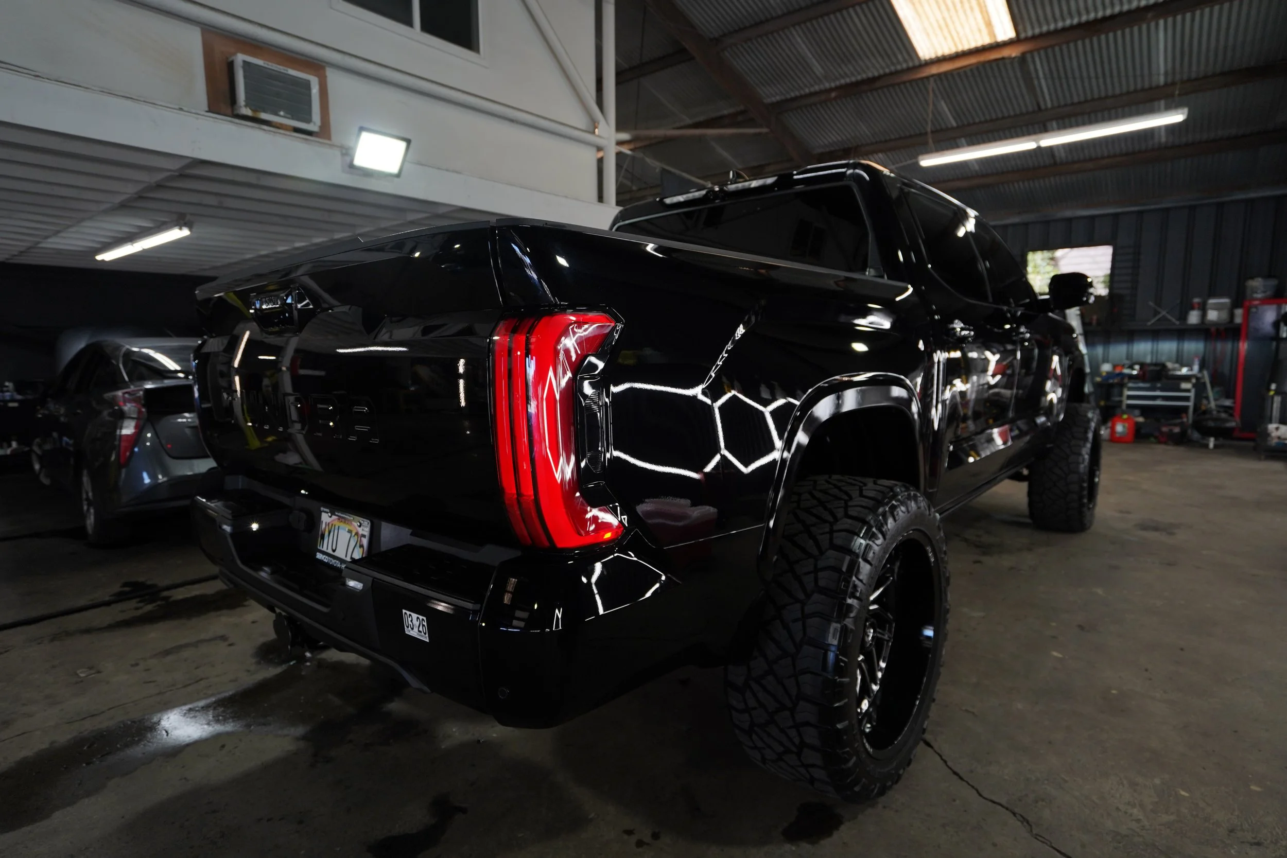 Black pickup truck with large, off-road tires inside a garage or warehouse.