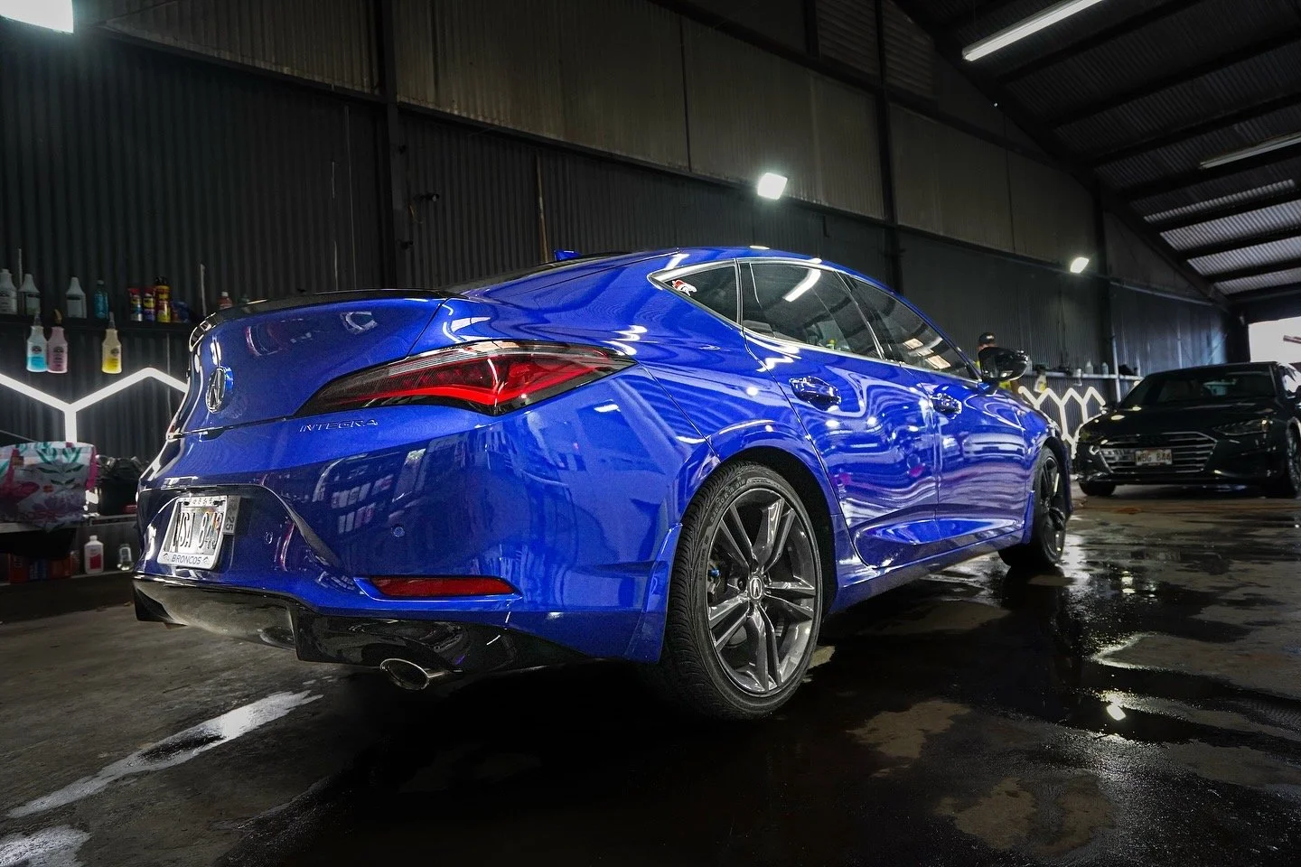 A shiny blue Acura Integra parked inside a car wash bay with other black cars visible in the background.