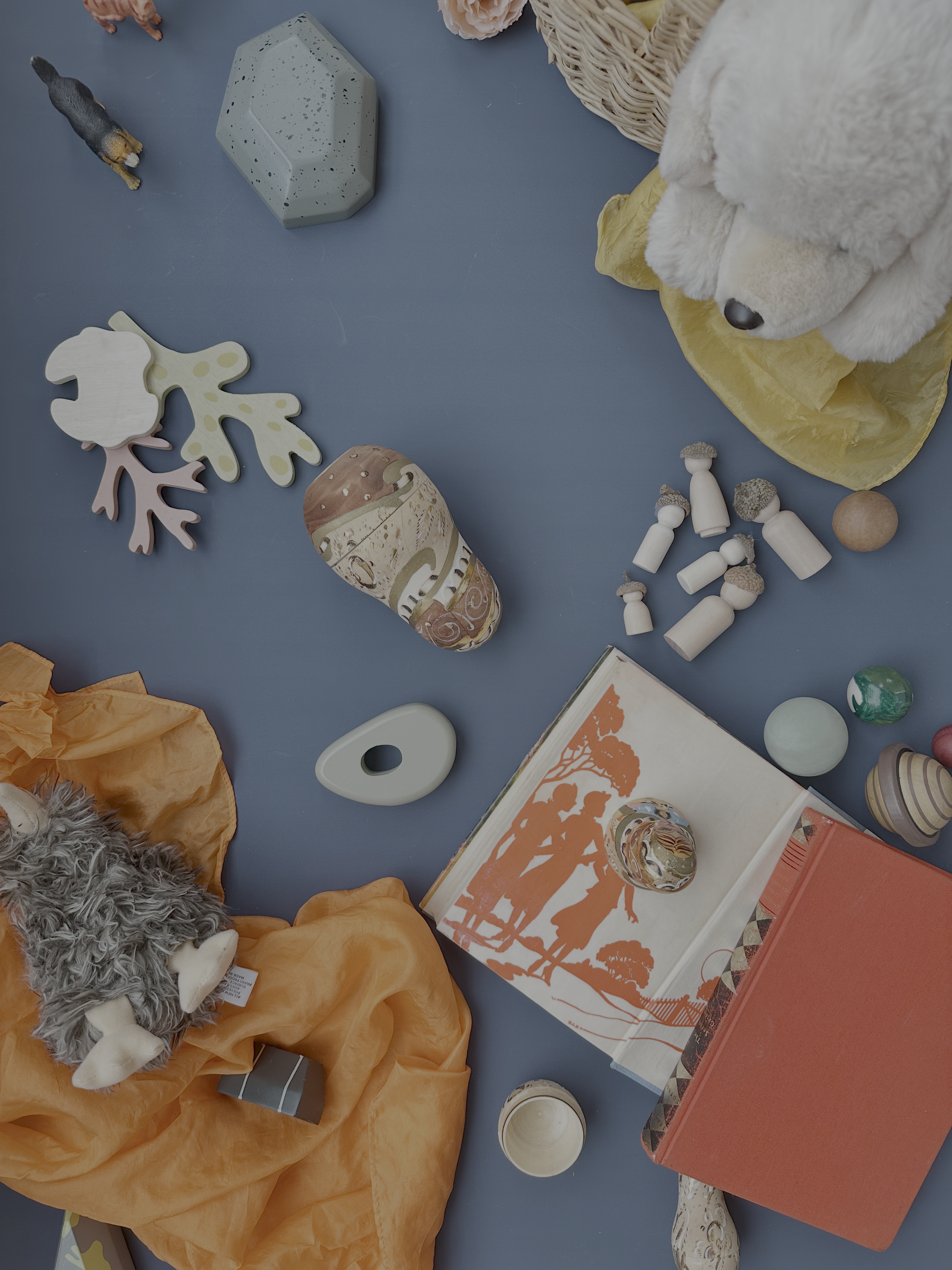 Various toys and objects scattered on a blue surface, including stuffed animals, wooden figures, decorative stones, and a scrapbook.