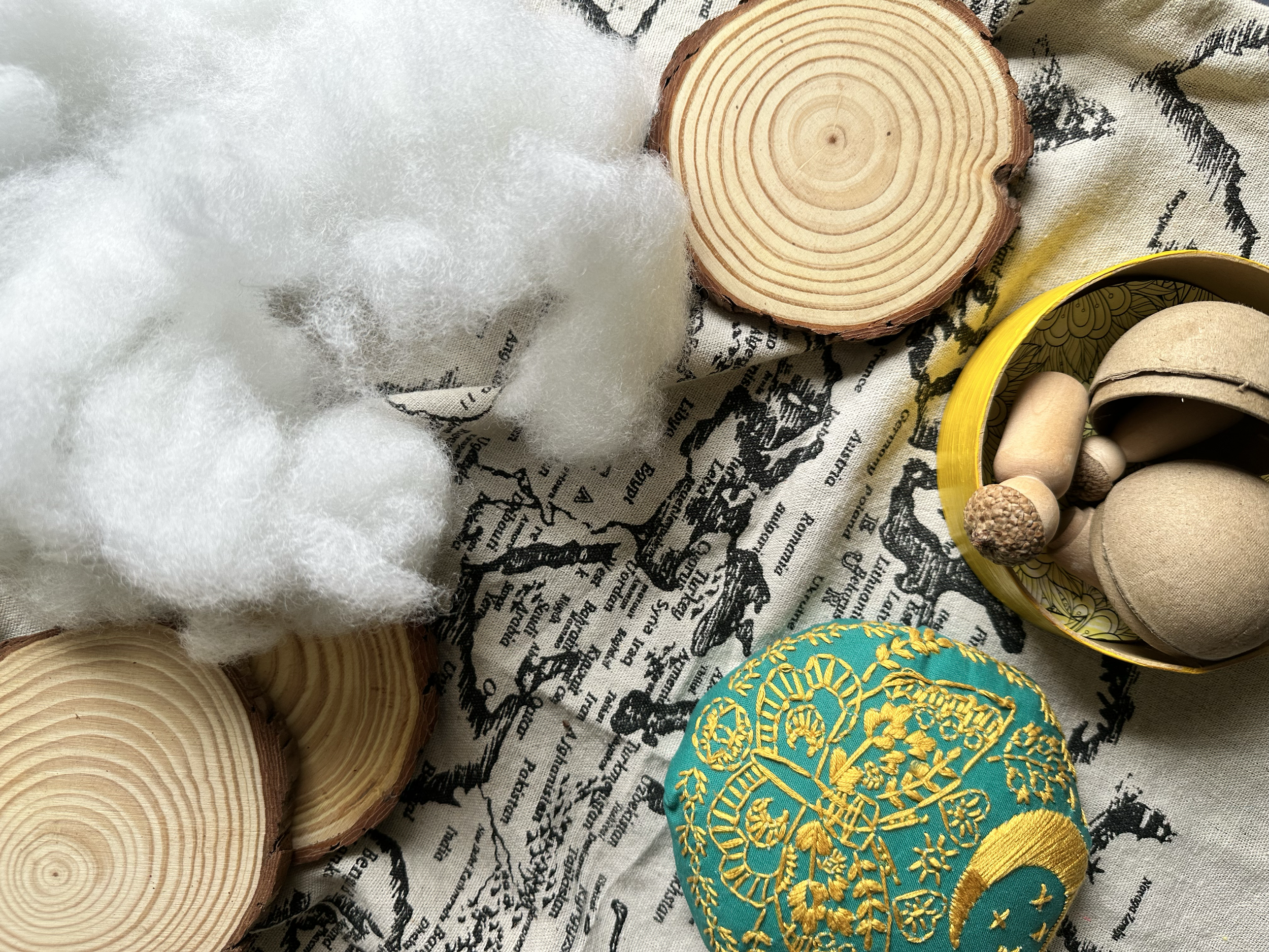 Assorted craft items including white fluffy stuffing, cut tree rings, a container of wooden and cork caps, and an embroidered fabric piece on a printed black and white fabric.