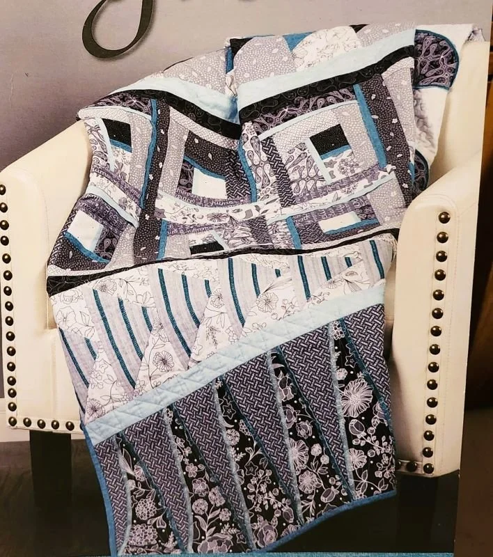 Bloom and Grow quilt draped over a chair, featuring modern quilt blocks in gray, blue, and floral fabrics.