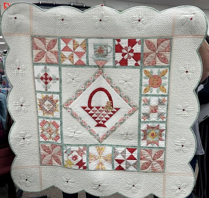 El’s Kitchen sampler quilt featuring a basket centerpiece and decorative patchwork blocks arranged in a soft, vintage-inspired layout.