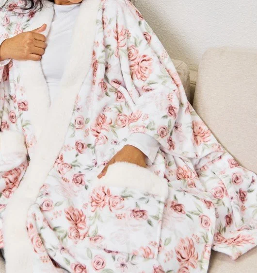 Person wearing a floral Cuddle Up Wrap made from plush fabric with soft white trim, draped comfortably for warmth.