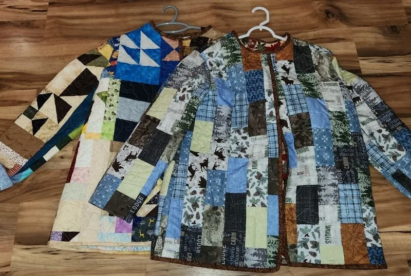 Quilted Laura Jackets made from patchwork fabric blocks, displayed on hangers with long sleeves and button fronts.