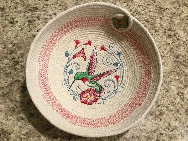 Rope basket sewing project featuring a round fabric bowl with embroidered hummingbird and decorative stitching