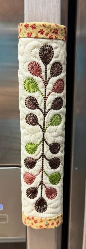Machine-embroidered fabric panel featuring a vertical arrangement of colorful flowers, leaves, and decorative stitching.