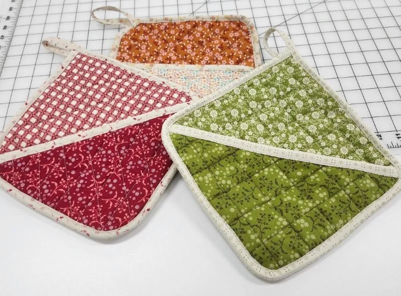 Colorful quilted fabric hot pad pockets in red, orange, and green patterns, displayed together as a sample serger project.