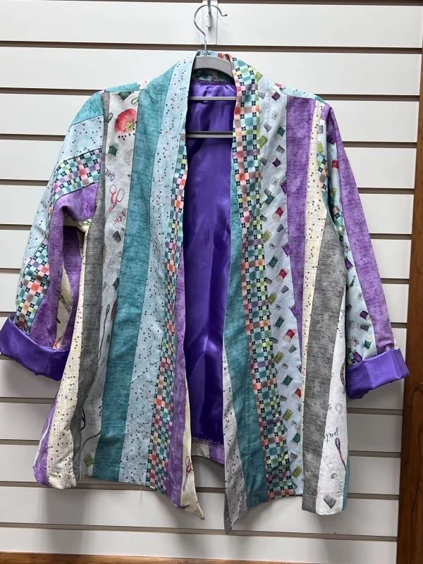 Colorful handmade jacket featuring vertical strips of patterned fabric in teal, purple, blue, and gray, with purple cuffs and front trim.
