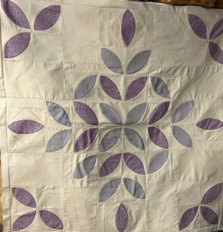 Mini Citrus quilt block featuring a circular floral-inspired design made from curved purple and lavender fabric pieces against a light cream background.