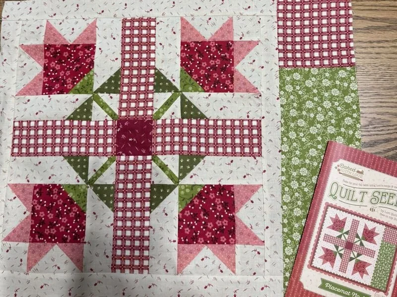 Quilted placemat featuring red, pink, green, and white patchwork blocks with floral star designs, displayed beside a Riley Blake quilt pattern.
