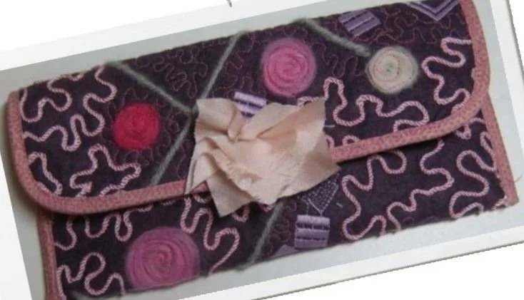 Handmade purple and black textured fabric clutch featuring decorative stitching, swirling patterns, and a contrasting fabric closure.