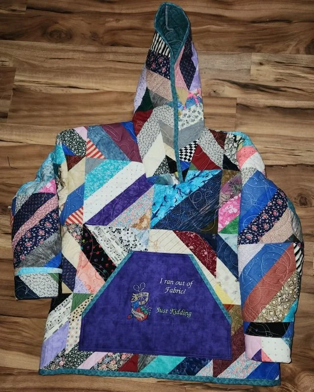 Handmade quilted hoodie featuring colorful geometric patchwork in shades of blue, purple, teal, and white, with a matching patchwork hood.