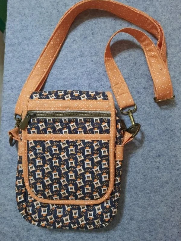 Handmade navy blue and cream patterned crossbody bag featuring tan handles, a front zippered pocket, decorative trim, and an adjustable shoulder strap.