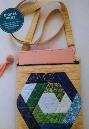 Handmade crossbody bag featuring a colorful blue, green, and white hexagon log cabin quilt pattern, a pink zippered top, and tan shoulder straps.